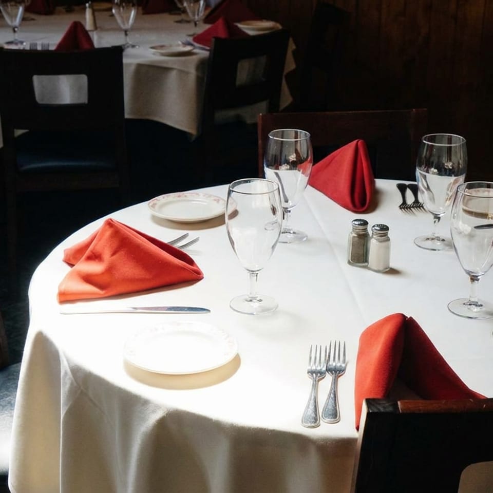 Elegant restaurant dining room with a white-tableclothed table, red folded napkins, glassware, plates, and silverware.